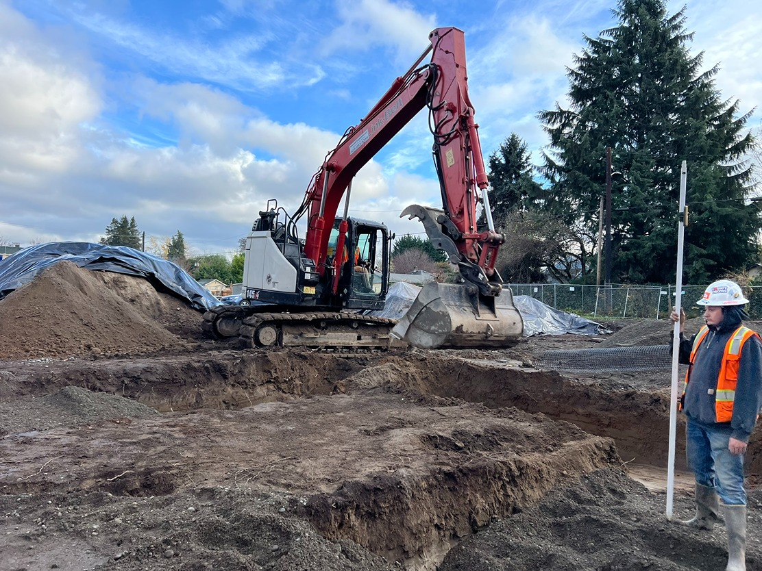 Excavator digging a foundation trench at a residential work site with a surveyor nearby
