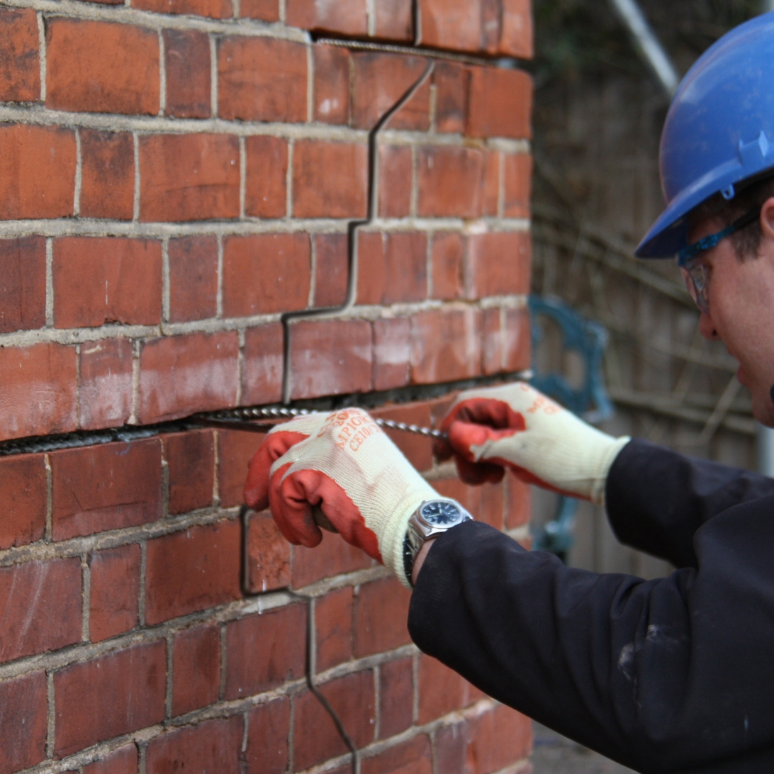 Mason repairing cracked mortar joints in a red brick Toronto wall