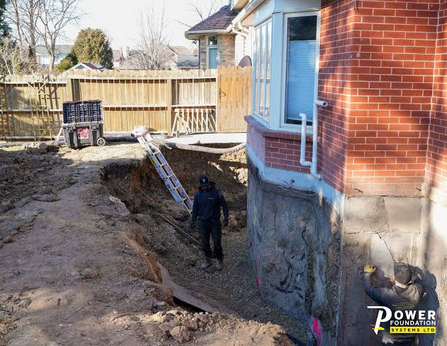 Crew working in an excavated foundation trench beside a brick Toronto home