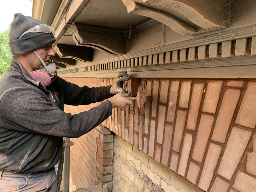 Mason removing deteriorated brick from a decorative Toronto exterior wall during restoration